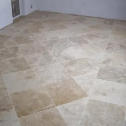 Jasne, kwadratowe płytki podłogowe ułożone w romby, z widoczną teksturą kamienia i fugami w odcieniu zbliżonym do koloru płytek.