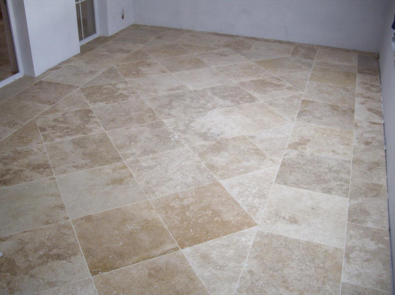 Jasne, kwadratowe płytki podłogowe ułożone w romby, z widoczną teksturą kamienia i fugami w odcieniu zbliżonym do koloru płytek.