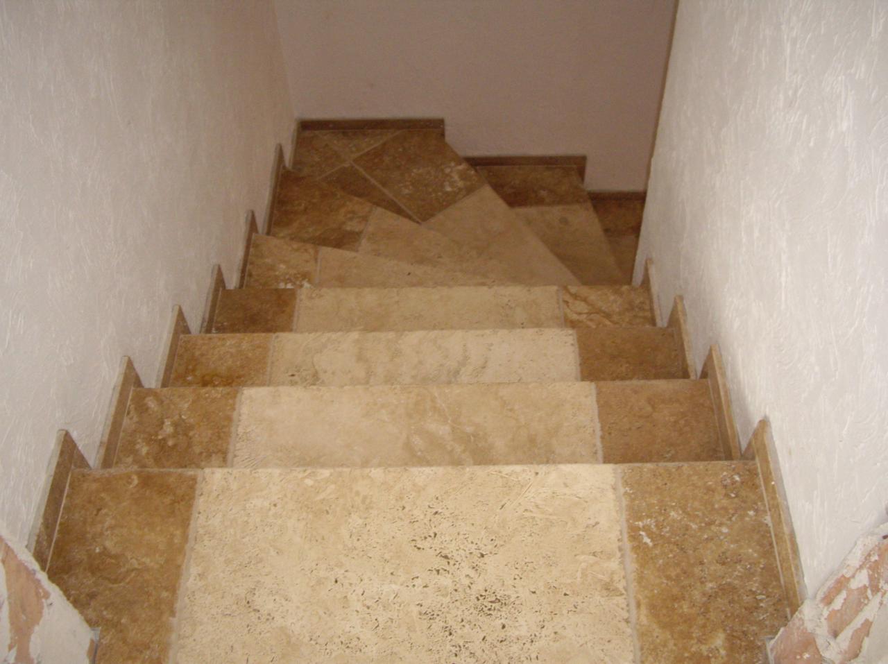 Schody wyłożone płytkami imitującymi trawertyn, widok z góry na dół, ściany wykończone jasnym tynkiem strukturalnym.