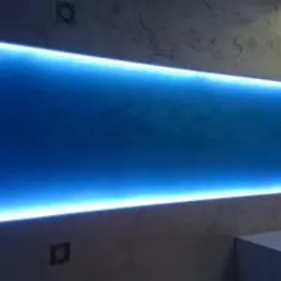 Podświetlony panel dekoracyjny w łazience w Bieczu, z efektem niebieskiego światła, zamontowany nad wanną, na tle ściany z dekoracyjnym tynkiem.