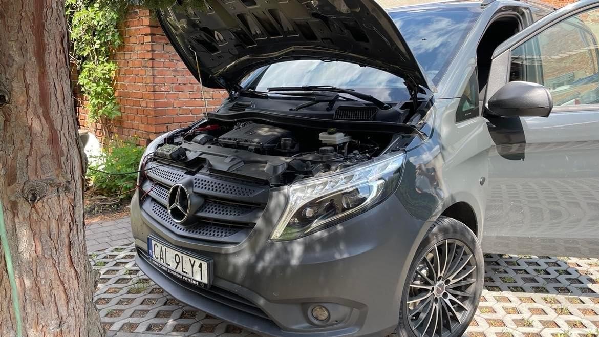 Szary Mercedes Vito z otwartą maską na zewnątrz, widoczny silnik i podłączony prostownik do akumulatora.