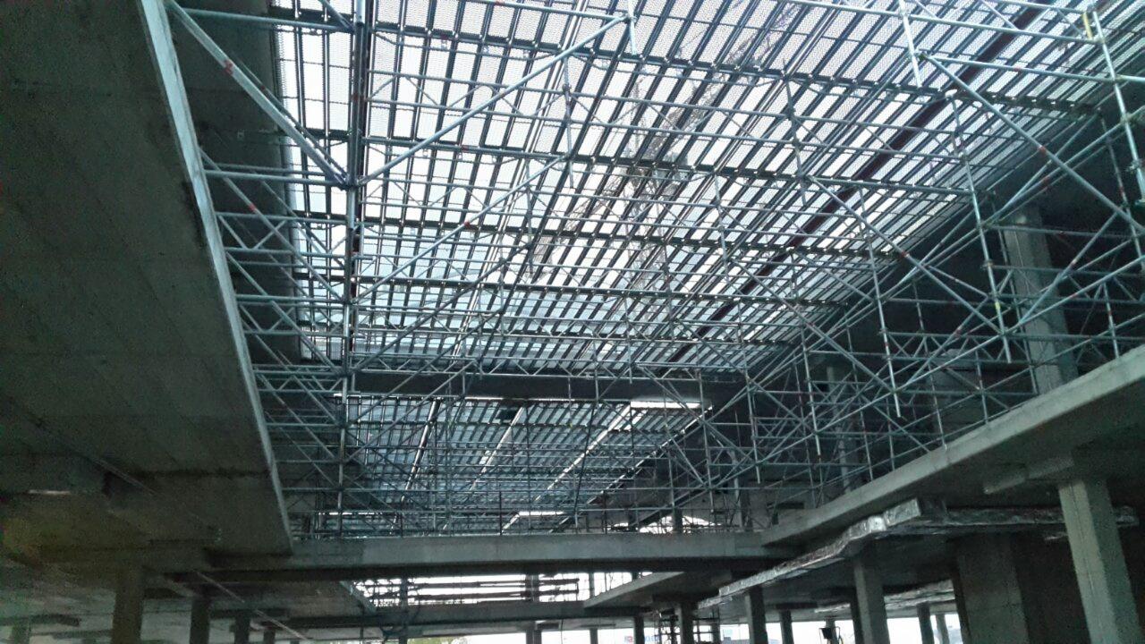 Konstrukcja rusztowania pod dachem budynku w trakcie budowy, widok od dołu, metalowe elementy tworzą skomplikowaną siatkę.