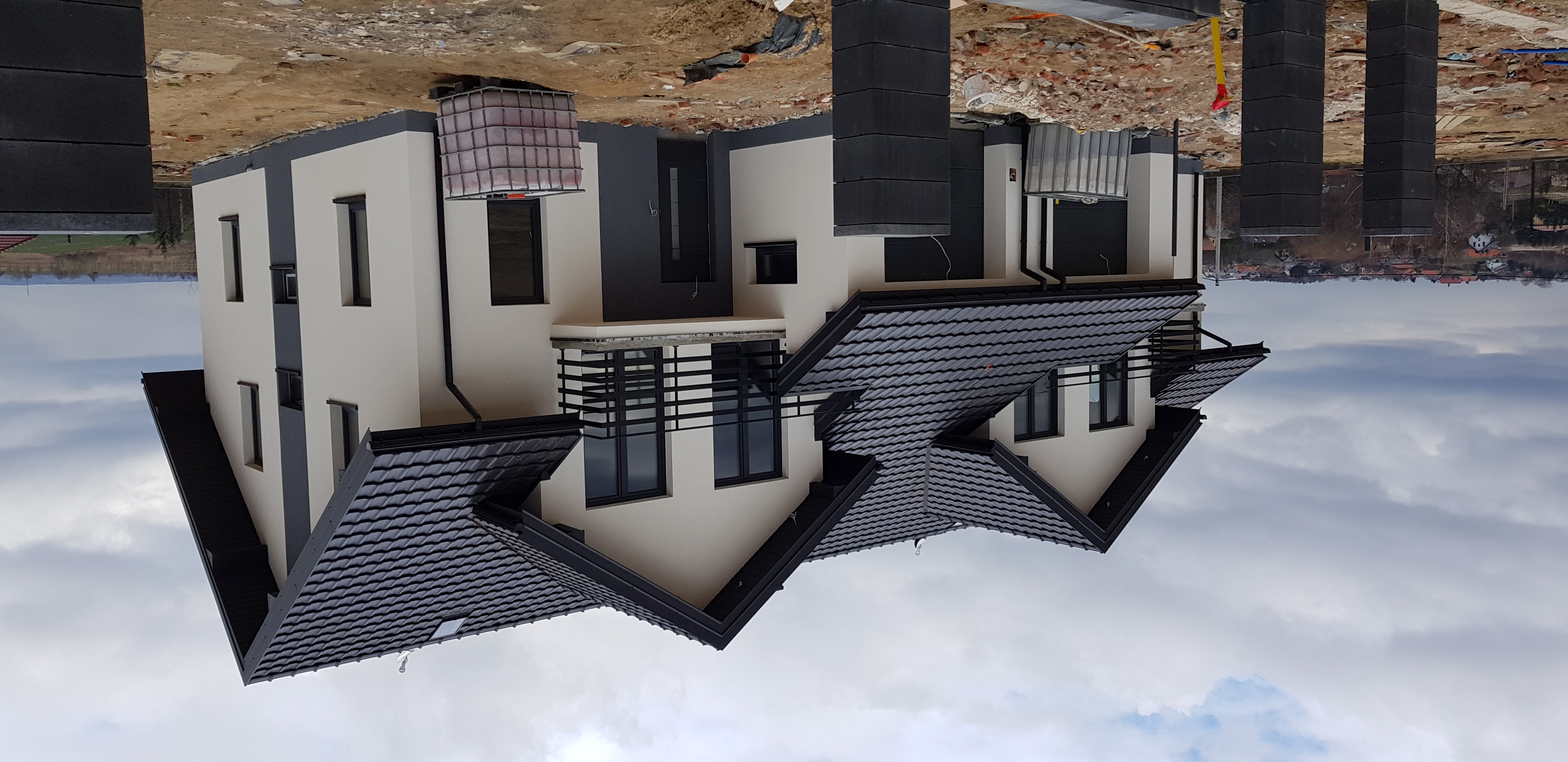 Nowoczesny dom jednorodzinny z czarną dachówką i elementami elewacji w odcieniach szarości, widoczny z zewnątrz, z terenem w trakcie prac wykończeniowych.