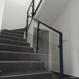 JURA-TECH - Nowoczesna balustrada szklana z czarnymi profilami na schodach z szarymi płytkami, widok z dołu, minimalistyczne wnętrze.