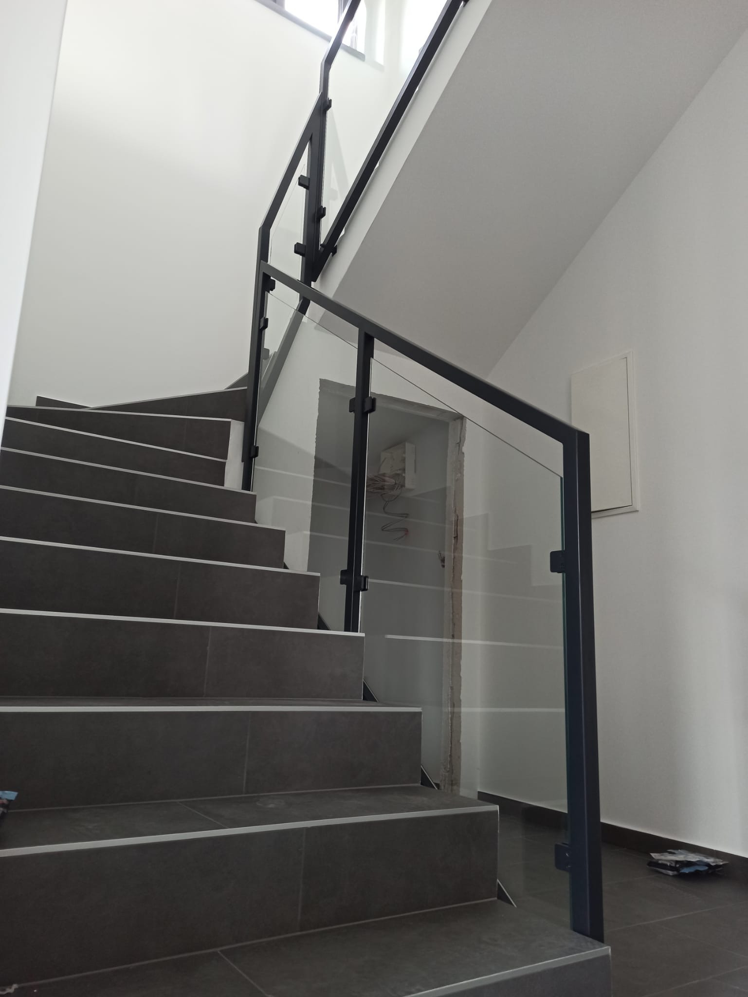 Nowoczesna balustrada szklana z czarnymi profilami na schodach z szarymi płytkami, widok z dołu, minimalistyczne wnętrze.