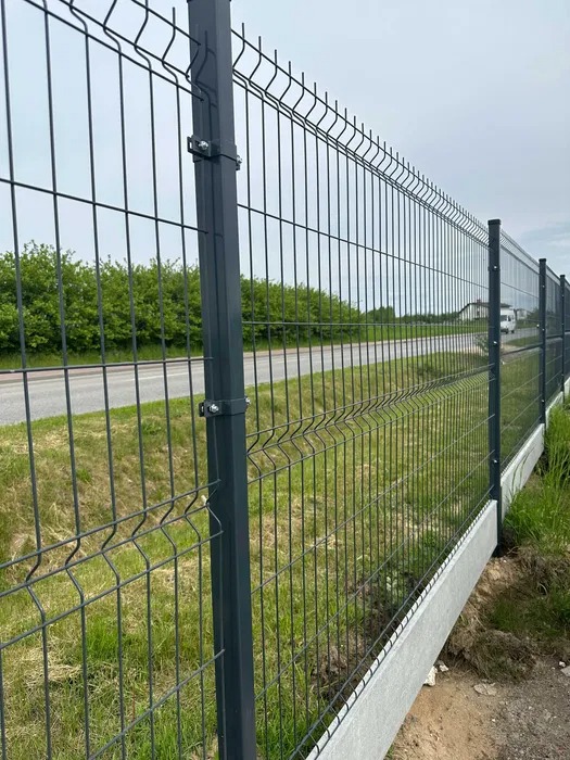 Nowoczesne ogrodzenie panelowe z podmurówką betonową, widok z bliska na słupki i siatkę, zieleń w tle, szara kolorystyka.