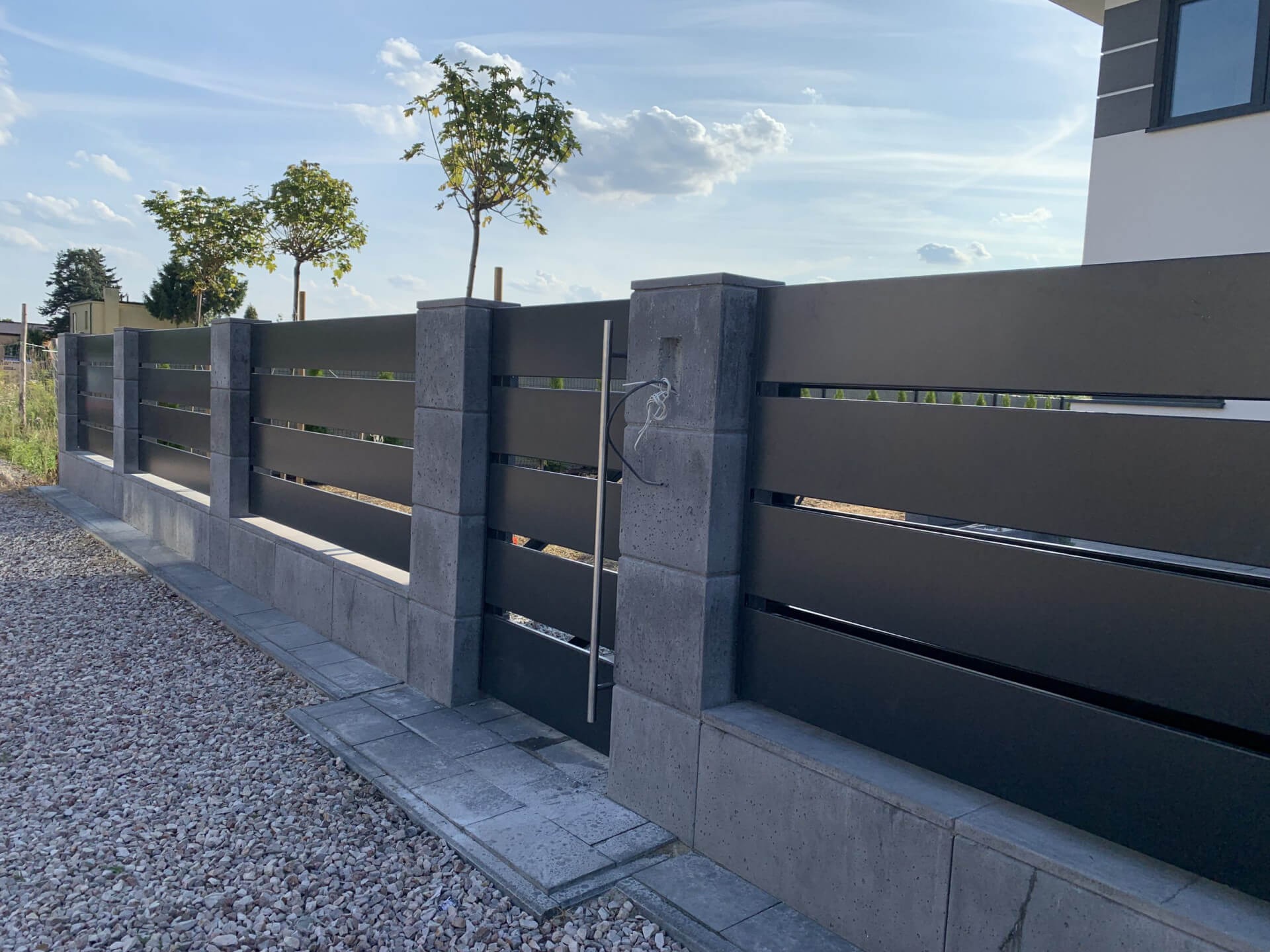 Nowoczesne ogrodzenie panelowe z bramką, szare słupki z betonu architektonicznego, Myszków. Poziome, metalowe przęsła w kolorze antracytu.