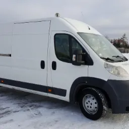 Biały samochód dostawczy typu bus na śniegu, widok z boku, z metalowym uchwytem na bocznych drzwiach i anteną na dachu.