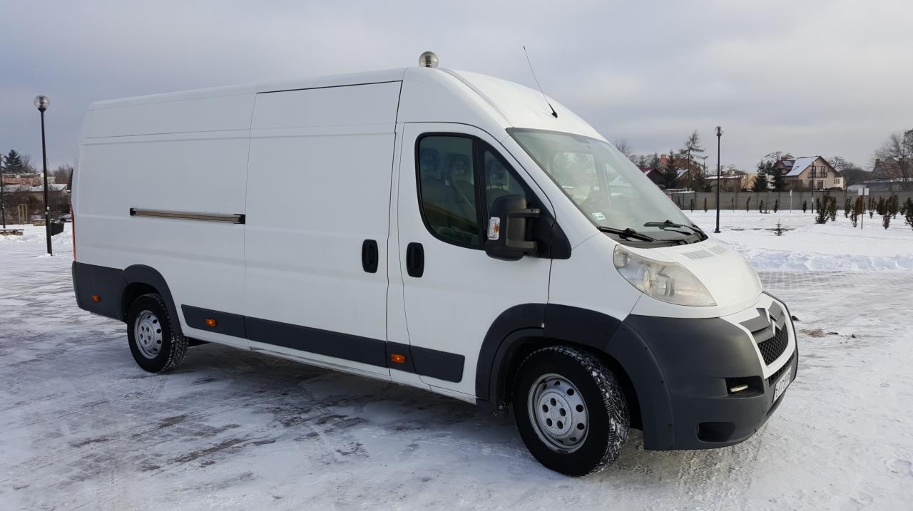 Biały samochód dostawczy typu bus na śniegu, widok z boku, z metalowym uchwytem na bocznych drzwiach i anteną na dachu.