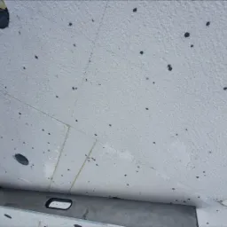 Biały sufit z widoczną strukturą i ciemnymi punktami, poziomowany przy użyciu poziomicy, widoczna dłoń.