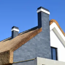 Fragment dachu z trzciny i łupka z dwoma kominami z szarego łupka z białymi detalami na tle błękitnego nieba.