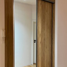 FHU JACK - Szafa wnękowa z przesuwnymi drzwiami lustrzanymi i drewnianym wykończeniem, oświetlona listwą LED, na tle jasnego wnętrza z parkietem.