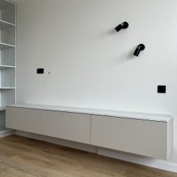 FHU JACK - Minimalistyczny salon: beżowa szafka RTV z marmurowym blatem, czarne lampy punktowe na białej ścianie, drewniana podłoga. Nowoczesne wykończenie wnętrza.