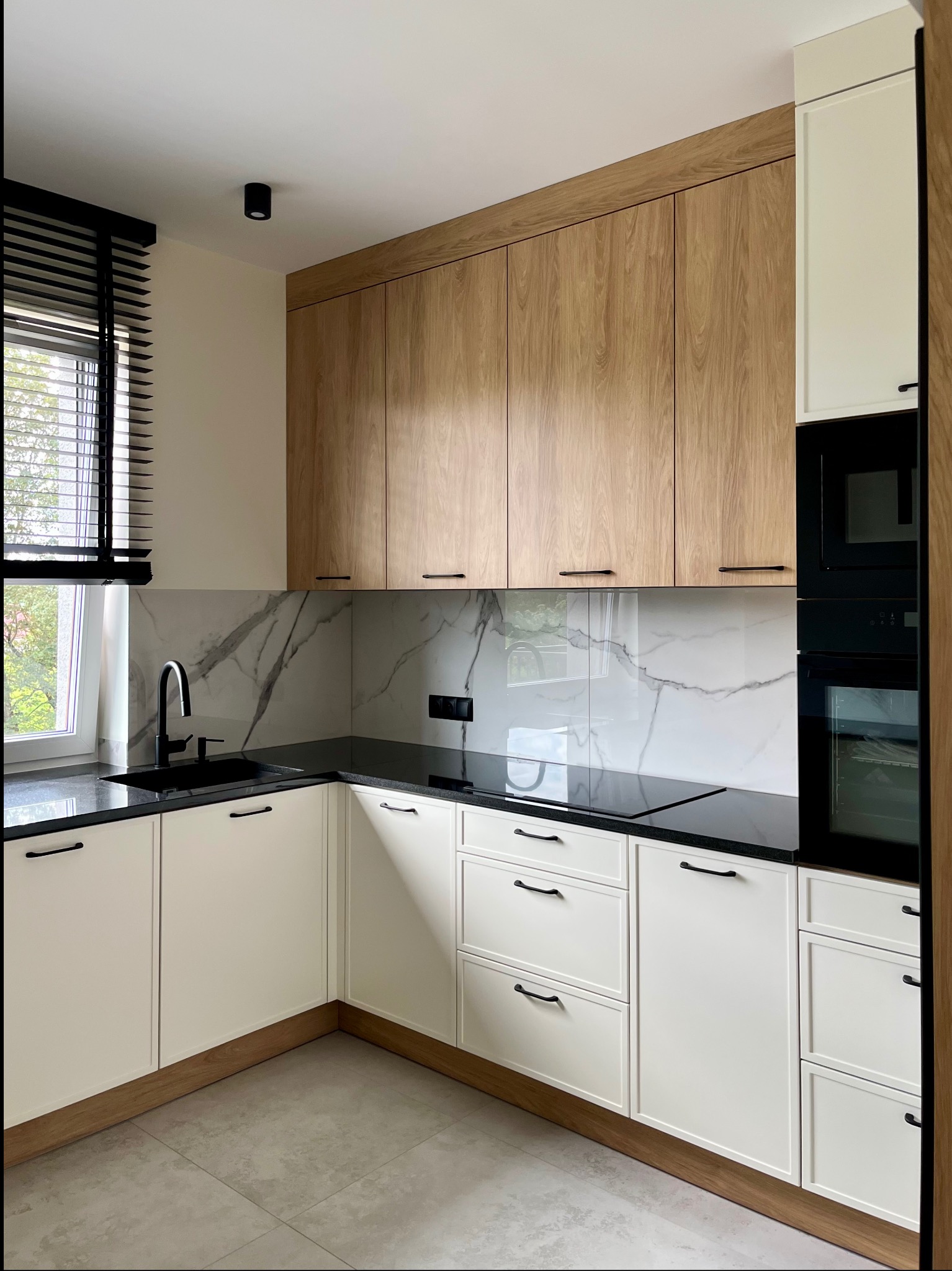 Nowoczesna kuchnia z białymi szafkami, drewnianymi górnymi szafkami i czarnym blatem. Minimalistyczny design z marmurowym backsplash.