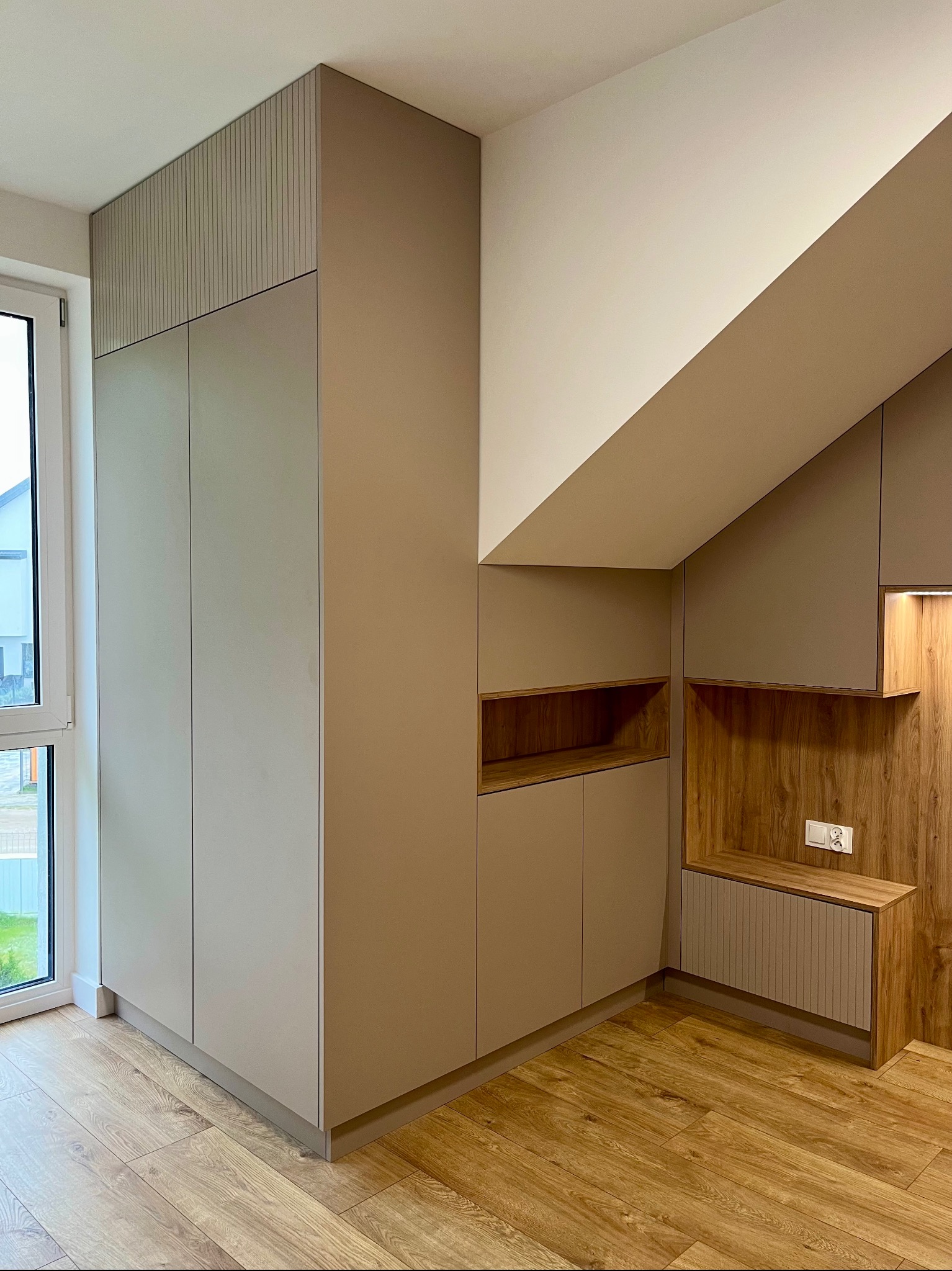 Funkcjonalna szafa wnękowa z drewnianymi akcentami, dopasowana do skosu dachu w Olsztynie. Nowoczesny design i optymalne wykorzystanie przestrzeni.