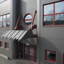 Fasada budynku firmy z elementami dekoracyjnymi nawiązującymi do maszyn budowlanych: stylizowana łyżka na wysięgnikach nad wejściem, okrągłe okno, szare blaszane panele ścienne i czerwone ramy...