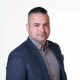 Mężczyzna w niebieskiej marynarce w kratę i koszuli w brązowo-białą kratę, z poszetką w kropki, na jasnym tle. Portret biznesowy.