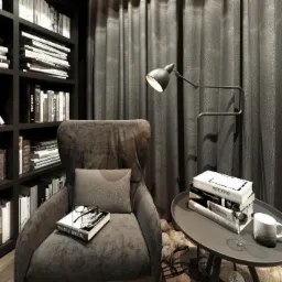 Szare, pluszowe krzesło z poduszką i książką, ustawione w rogu pokoju z ciemnymi zasłonami i regałem pełnym książek, oświetlone lampą stojącą.