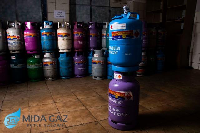 Kolorowe butle z gazem ustawione rzędami i w stos, z logo Mida Gaz w lewym dolnym rogu.