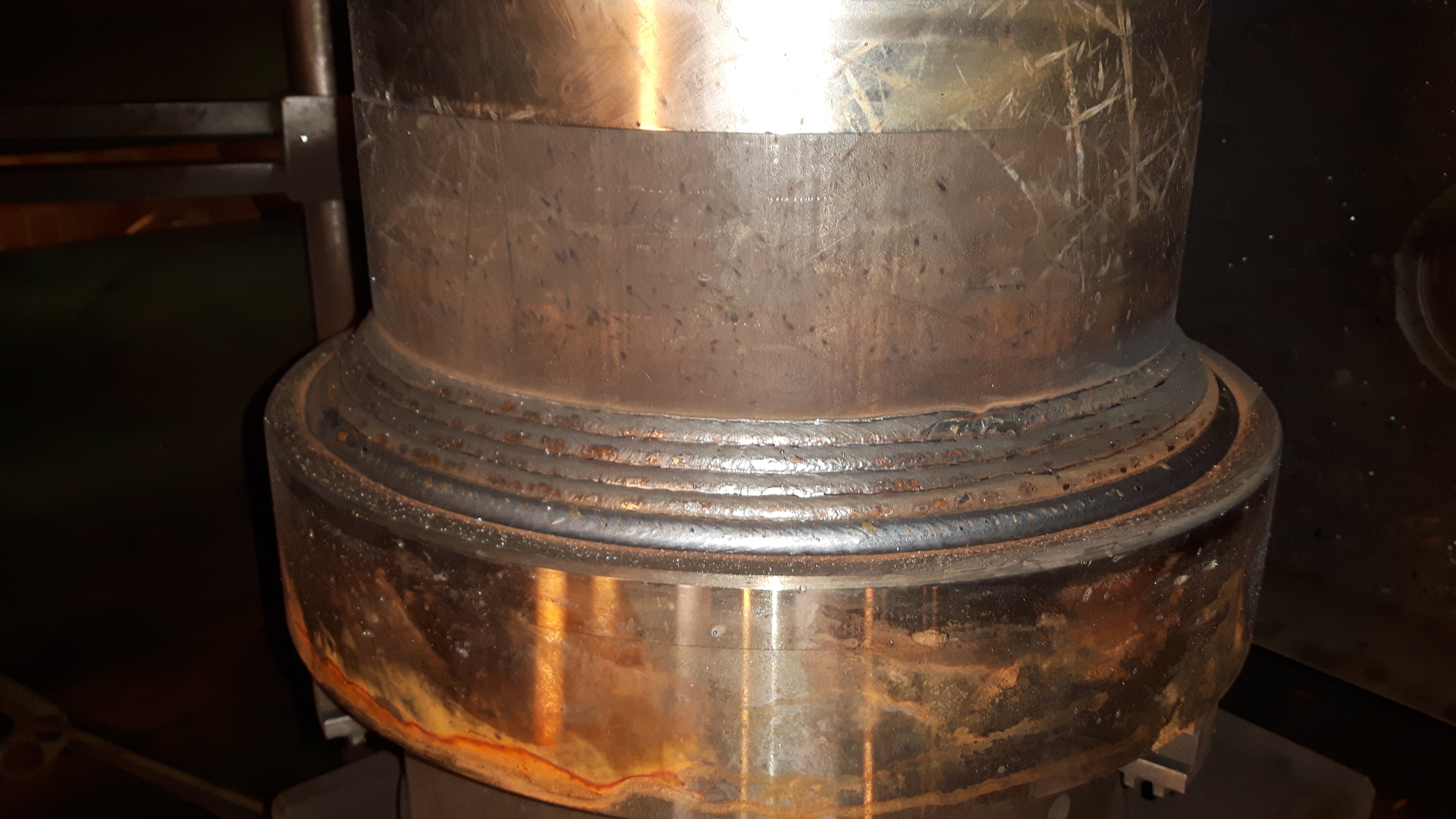 Metalowy element konstrukcyjny z widocznymi wieloma warstwami spoin, wykonany w procesie łączenia elementów. Widoczne ślady po spawaniu i obróbce metalu.