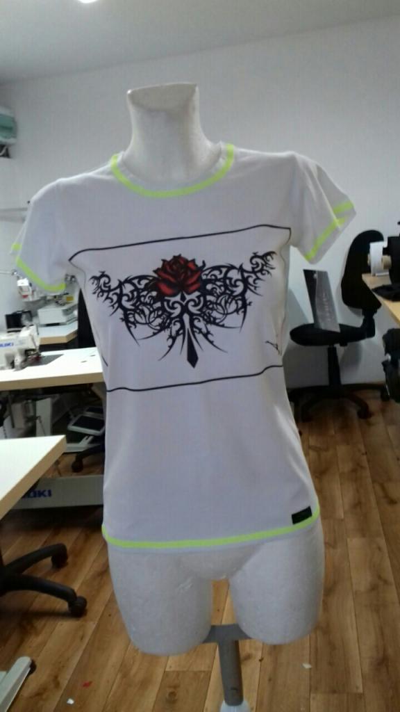 Biała koszulka z czarnymi paskami i wzorem róży na manekinie, wykończona neonowo-zielonymi detalami.