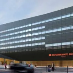 Wizualizacja zewnętrzna nowoczesnego, wielopiętrowego hotelu Renaissance Hotel z ciemną elewacją i równomiernie rozmieszczonymi oknami, widok z poziomu ulicy z przejeżdżającymi samochodami...