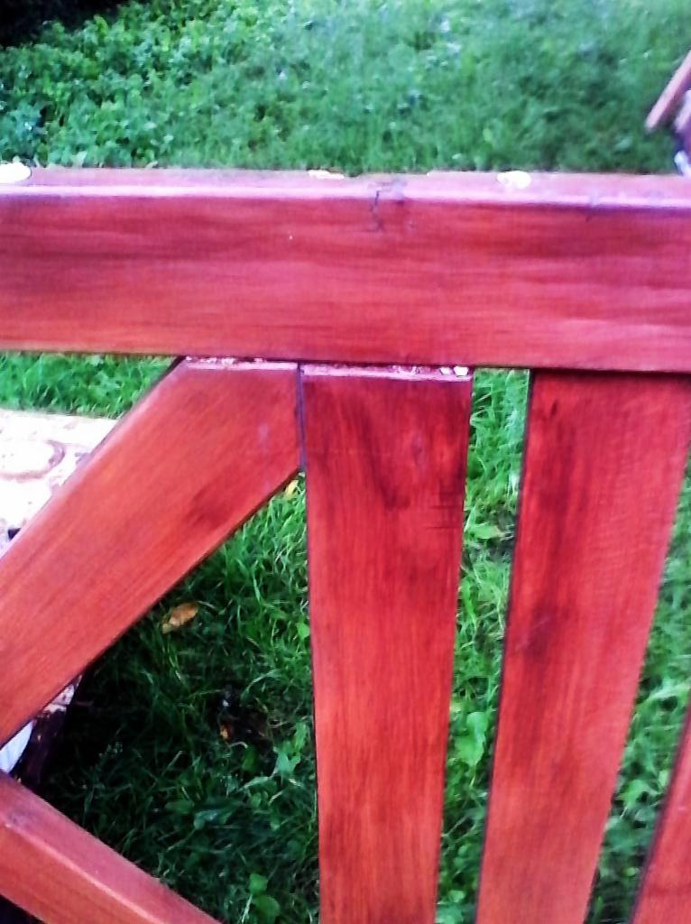 Fragment nowo pomalowanego, drewnianego płotu w kolorze mahoniowym, widoczny na tle zielonej trawy.