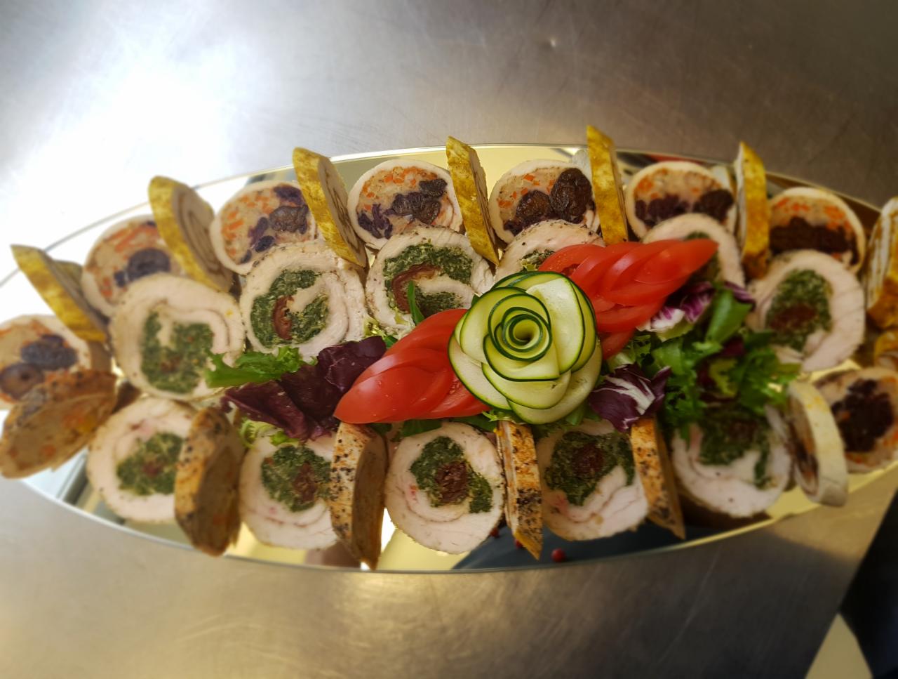 Dekoracyjnie ułożone roladki z kurczaka z różnymi nadzieniami, w tym szpinakiem i suszonymi pomidorami, na srebrnej tacy, ozdobione warzywami.