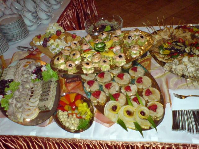 Bogato zastawiony stół z różnorodnymi przekąskami, w tym kanapeczkami, sałatkami i wędlinami, przygotowanymi na przyjęcie.