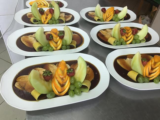 Elegancko zaaranżowane talerze z deserem owocowym: melon, pomarańcza, winogrona i truskawki w ciemnym sosie, ułożone na białych talerzach.