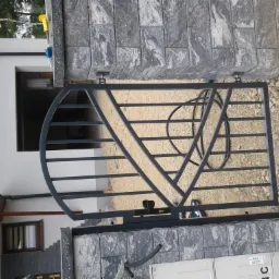 Metalowa brama wjazdowa z elementami dekoracyjnymi w kształcie półkola i trójkąta, zamontowana na murowanych słupkach z szarej kostki, widok z zewnątrz posesji.