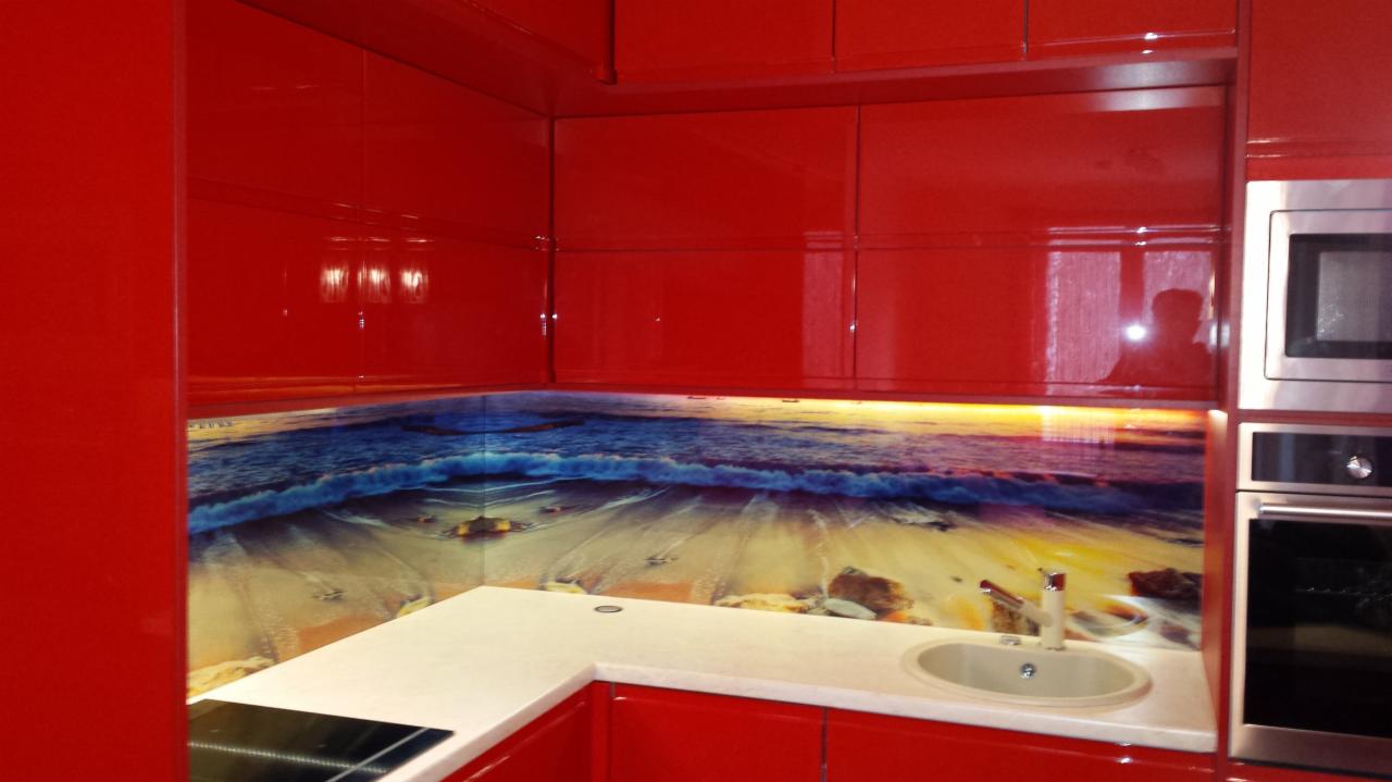 Czerwona kuchnia z lakierowanymi frontami i panelem szklanym z motywem plaży i morza nad blatem roboczym.