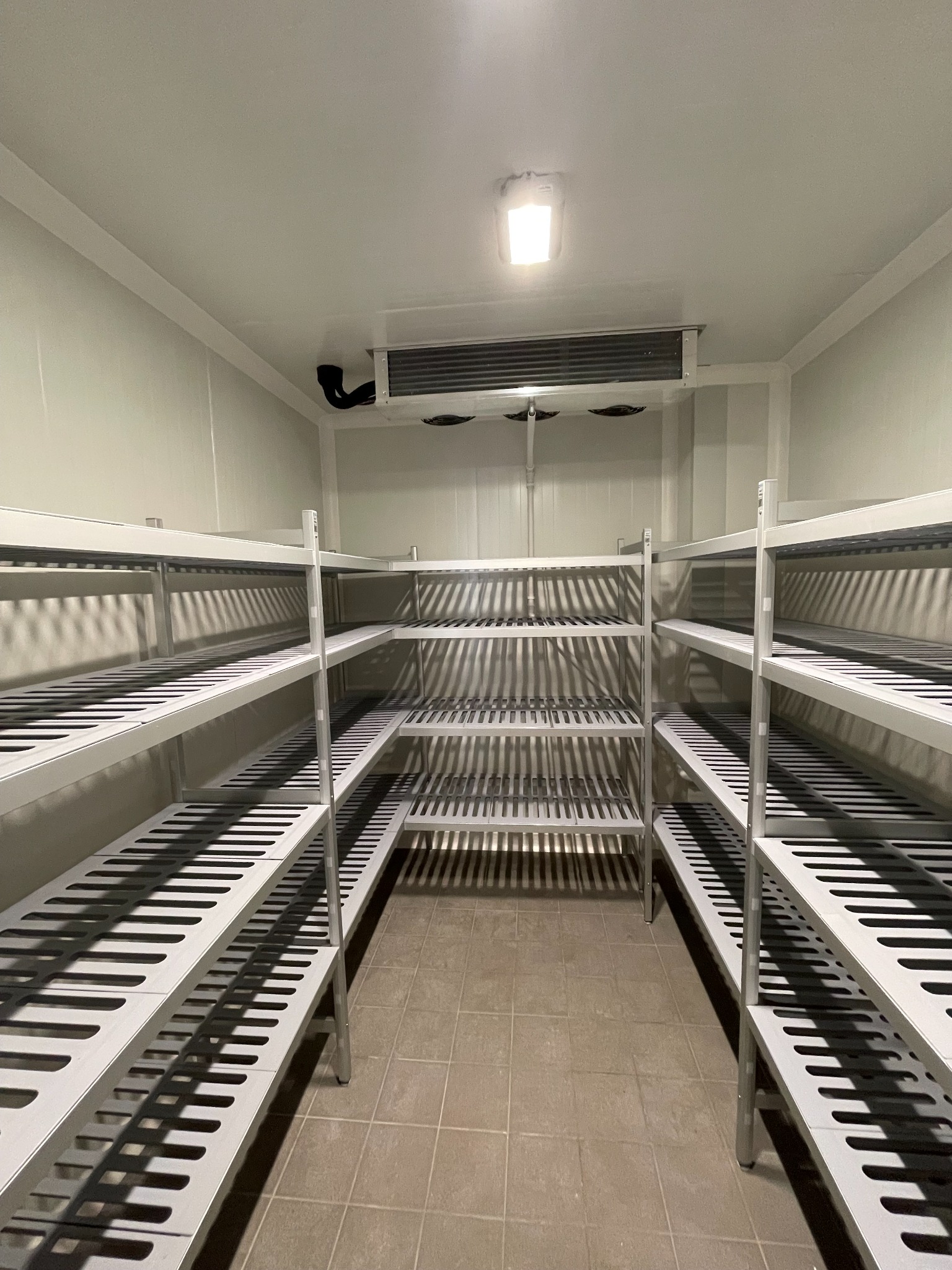 Pusta chłodnia z metalowymi regałami i klimatyzatorem w Ożarowie Mazowieckim, gotowa do przechowywania produktów.