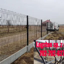 Nowo zamontowane czarne ogrodzenie panelowe z podmurówką betonową na nierównym terenie, widoczny samochód dostawczy w tle i częściowo nałożone logo z numerem telefonu.