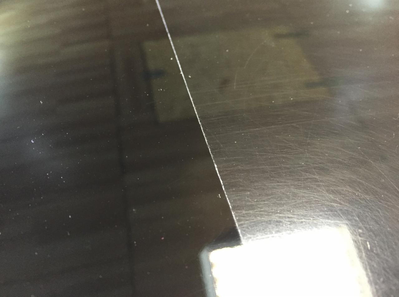 Błyszcząca, czarna powierzchnia zarysowanego lakieru samochodowego, oddzielona wyraźną linią od obszaru z minimalnymi uszkodzeniami.