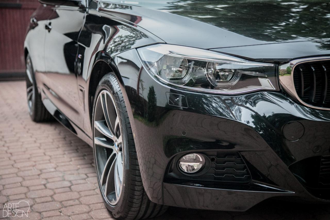 Błyszczący, czarny samochód marki BMW, widok na przedni reflektor, koło i fragment karoserii po detailingu, z odbiciami otoczenia na lakierze.