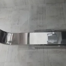 Panel prysznicowy ze stali nierdzewnej zamontowany na ścianie wyłożonej płytkami imitującymi beton w odcieniach szarości, widoczne dysze do hydromasażu.