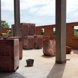 Wnętrze w trakcie budowy domu murowanego z widocznymi pustakami ceramicznymi Horl & Hartmann Coriso, betonowymi słupami nośnymi i częściowo wzniesionymi ścianami z otworami okiennymi.