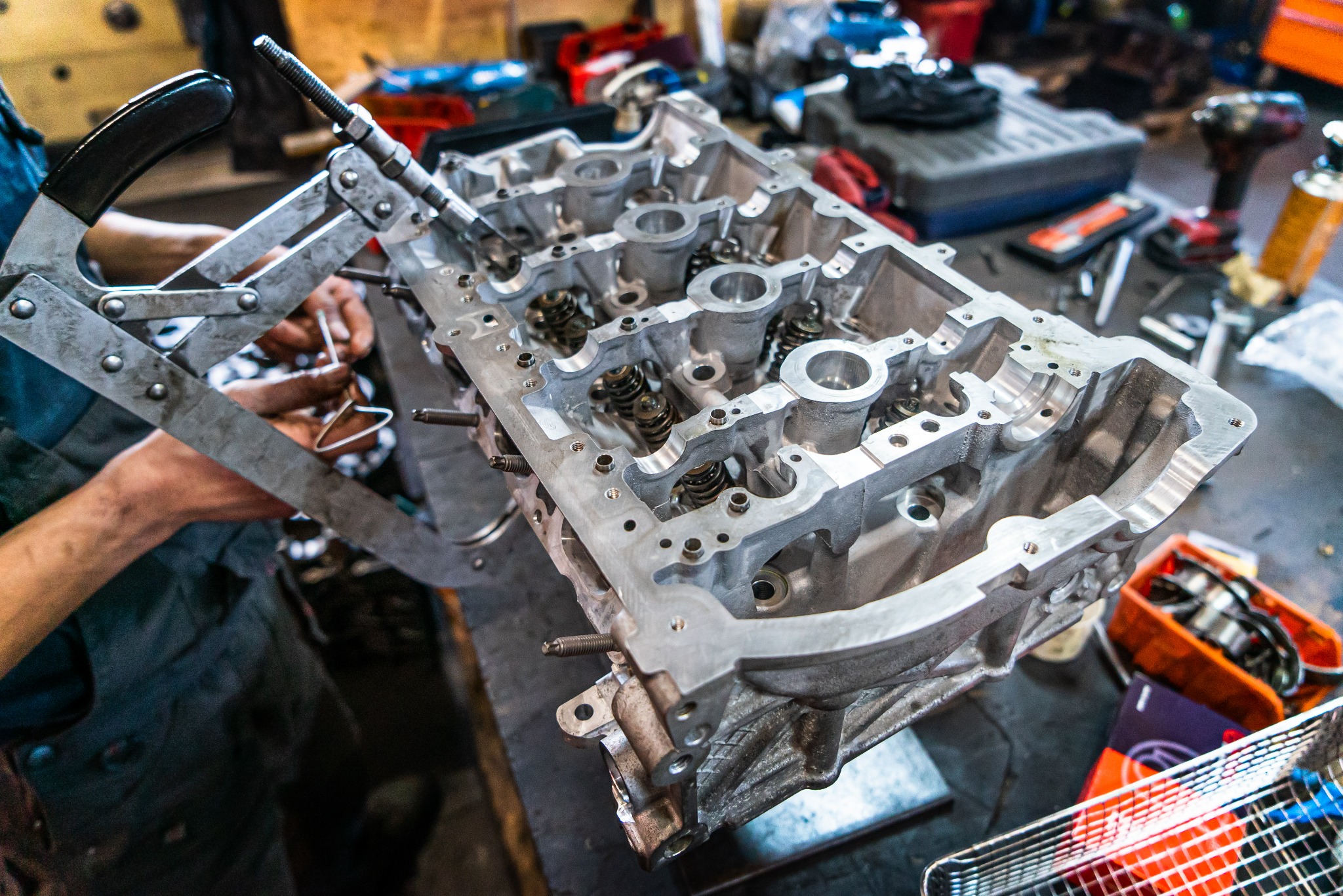 Demontaż sprężyn zaworowych z głowicy silnika za pomocą specjalistycznego narzędzia na warsztatowym stole.