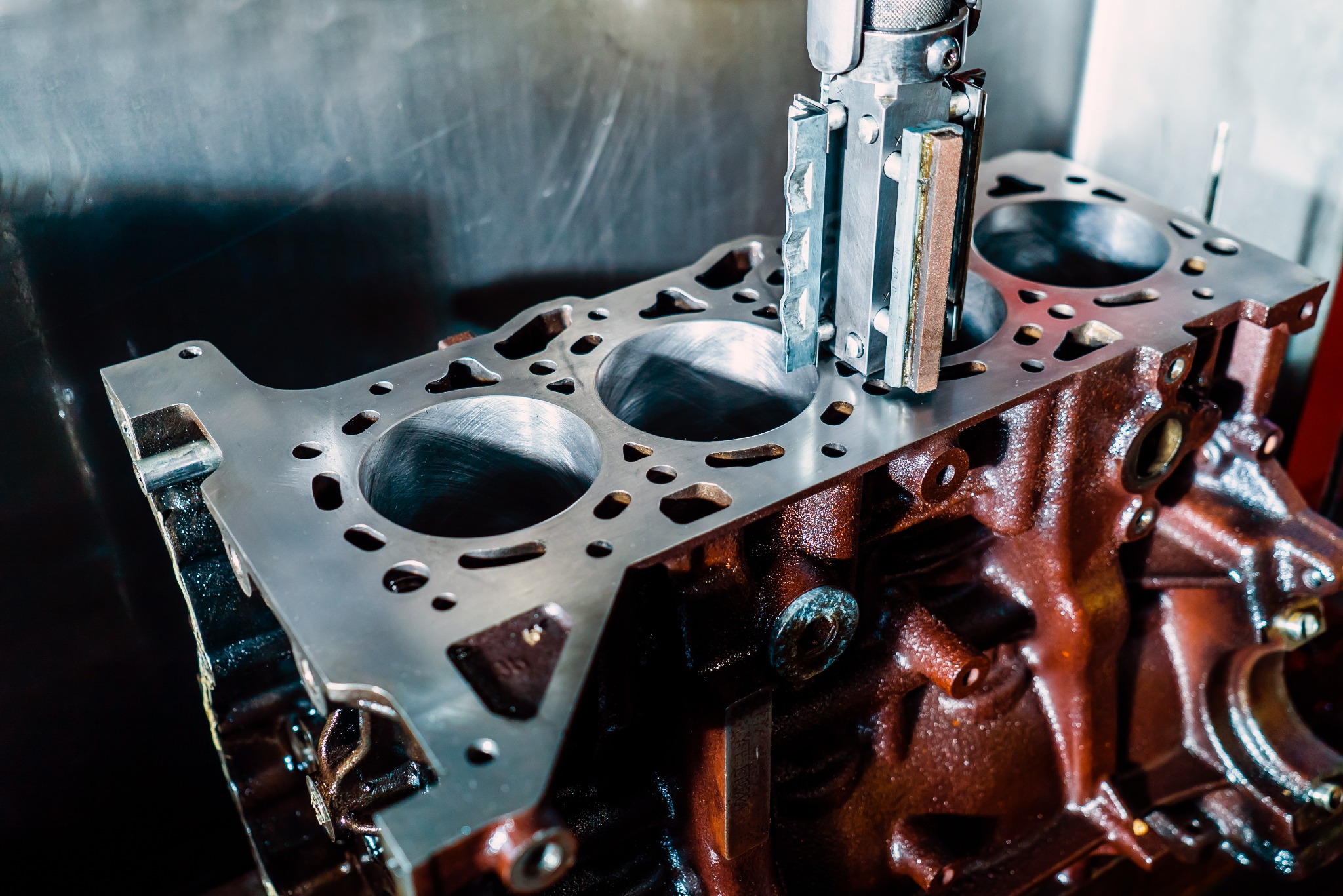 Blok silnika po honowaniu cylindrów, widoczne ślady obróbki i metalowe narzędzie.