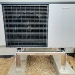 Zewnętrzna jednostka pompy ciepła Viessmann zamontowana na stalowej konstrukcji wsporczej, z widocznym fragmentem elewacji budynku i przygotowanym podłożem z kamyczków.