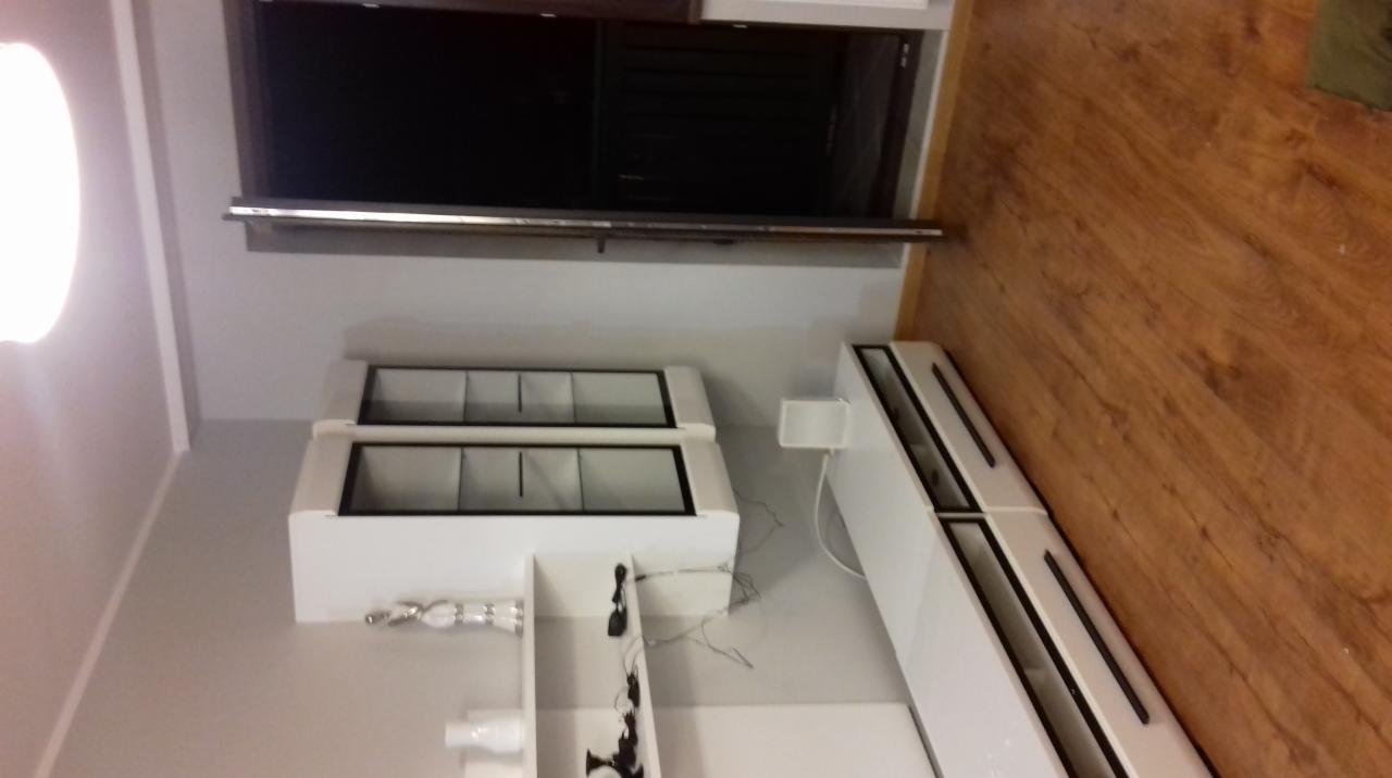 Nowoczesne, białe meble modułowe z czarnymi akcentami, zamontowane na szarej ścianie, z widoczną drewnianą podłogą i fragmentem czarnego okna.