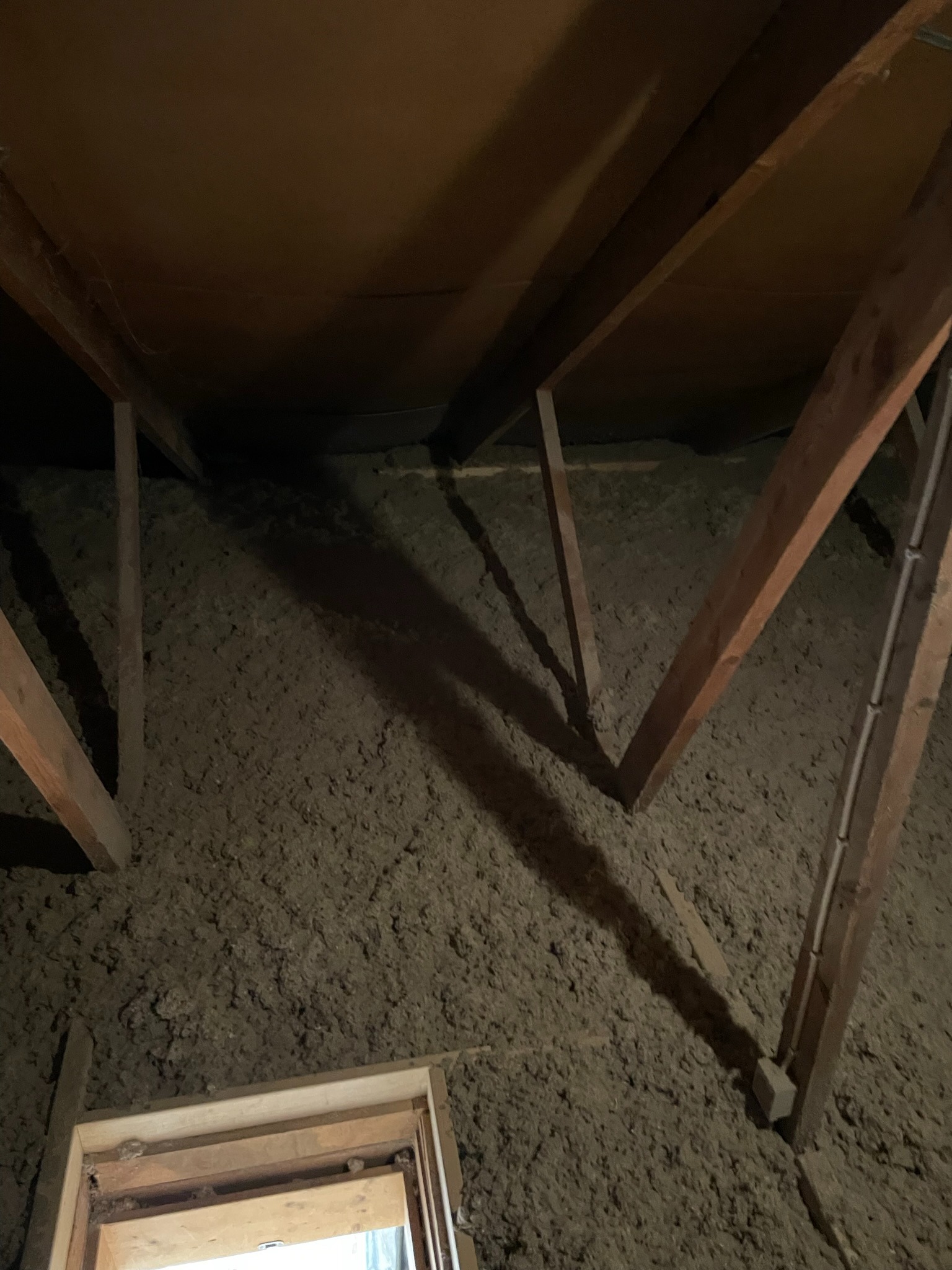 Poddasze z ociepleniem z wełny celulozowej, widoczne drewniane krokwie i fragment okna dachowego w dolnej części kadru.