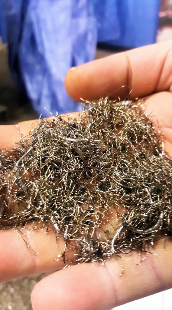 Garść drobnych, metalowych włókien w dłoni, prawdopodobnie pozostałości po obróbce, z widocznymi śladami brudu.