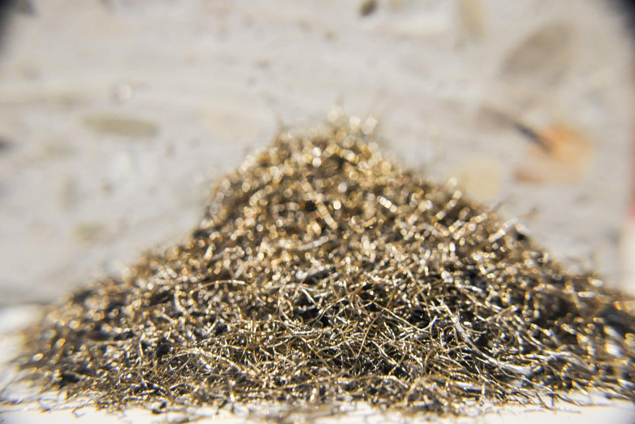 Makro ujęcie drobnych, metalowych włókien tworzących kopiec na jasnej powierzchni, z rozmytym tłem betonowym.