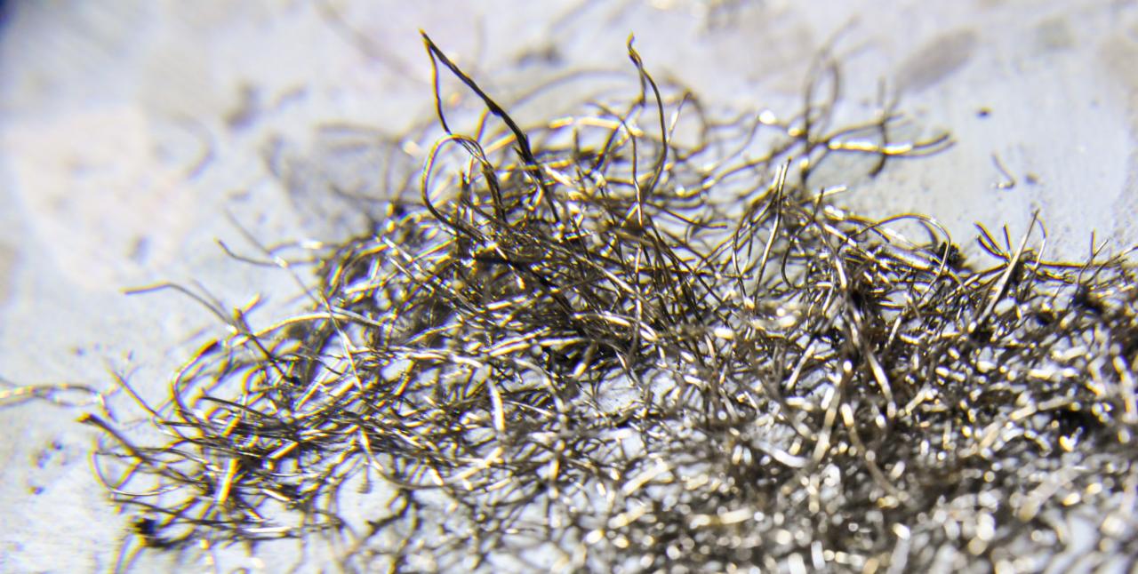 Makro zbliżenie na wiązkę cienkich, poskręcanych drutów metalowych na szarej powierzchni, przypominających włókna, z nieostrym tłem.