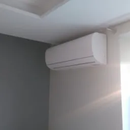 Biała jednostka wewnętrzna klimatyzacji zamontowana na szarej ścianie w pomieszczeniu w Rzeszowie, widoczny fragment sufitu z dekoracyjną listwą.