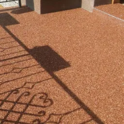 Bursztynowa, żywiczna posadzka balkonu w słoneczny dzień. Cień balustrady z motywem serca. Minimalistyczna kolumna w tle.