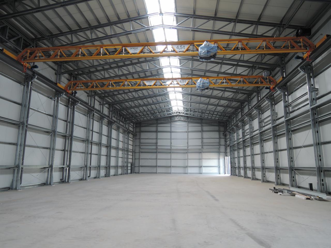 Wnętrze nowo wybudowanej hali z metalową konstrukcją szkieletową, widoczne żółte suwnice podwieszane i świetliki w dachu.