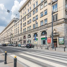 MIX - BUD WŁODARCZYK PAWEŁ - Elewacja kamienicy z oknami i klimatyzacją, widok z ulicy z przejściem dla pieszych i torami tramwajowymi. Na elewacji szyldy reklamowe i apteki.